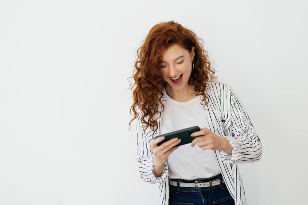 young redhead woman playing video games her phone watching video live stream cellphone laughing smiling looking mobile screen white background