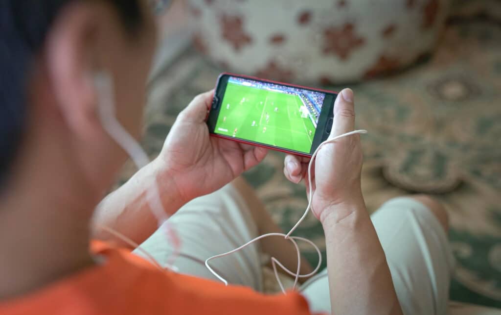 uomo che guarda lo streaming di calcio sportivo a casa sullo smartphone