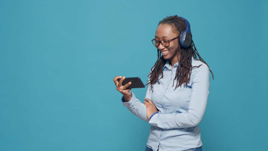 adulto joven viendo una película aplicación para teléfono inteligente usando auriculares inalámbricos escuchar programa de televisión película en línea red de internet disfrutando de un canal de televisión de comedia divertida usando un teléfono móvil