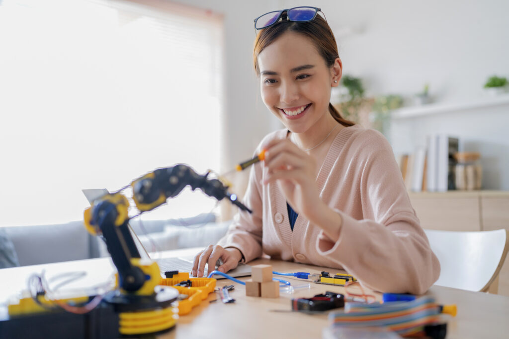 programmer wanita Asia pintar belajar lengan robot coding ai papan elektronik kabel batang uap dia mencoba menguji lengan robot otonomnya dengan sensor melalui platform arduino rumah